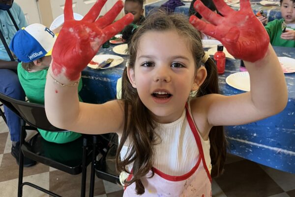 A child shows her paint-covered hands to the camera